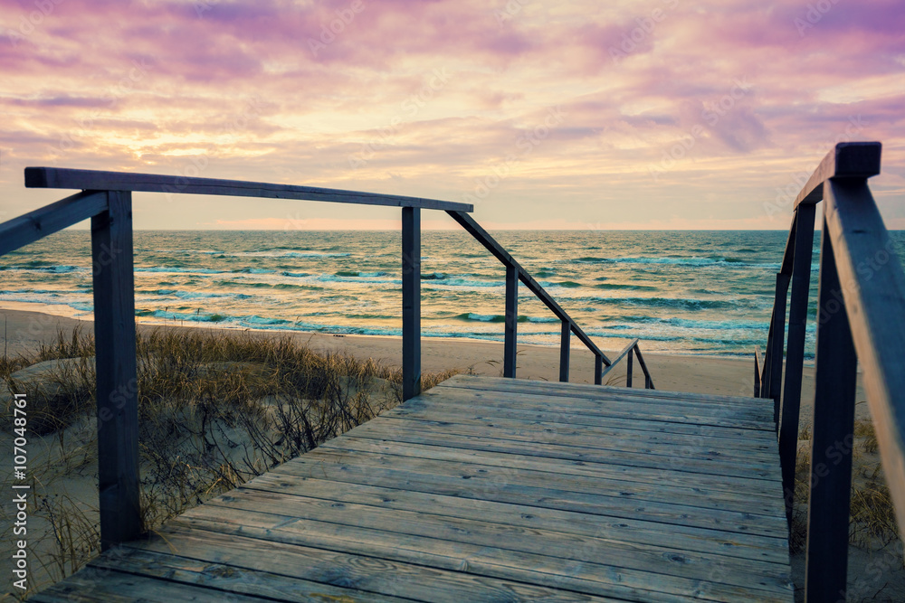 Fototapeta Wooden staircase with a handrail to the sea at sunset