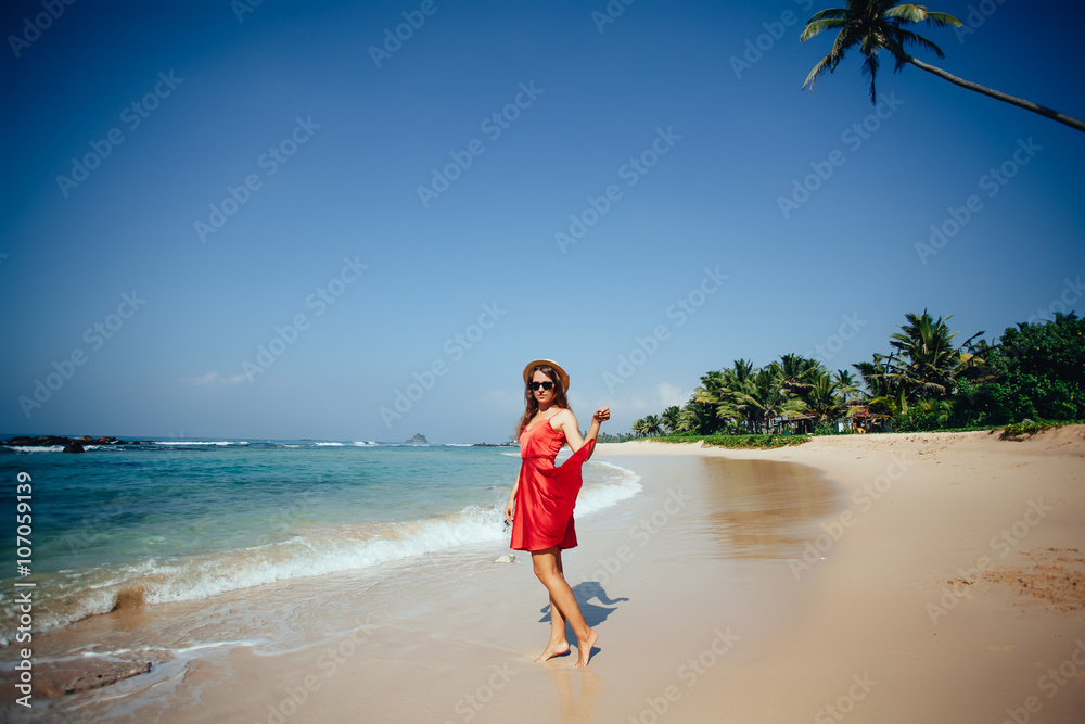Elegant Beautiful Woman in Red Dress and straw hat on the Beach.
