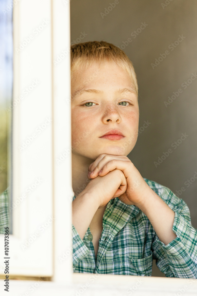 Boy with hands on chin near open window Boy with hands on chin near open window