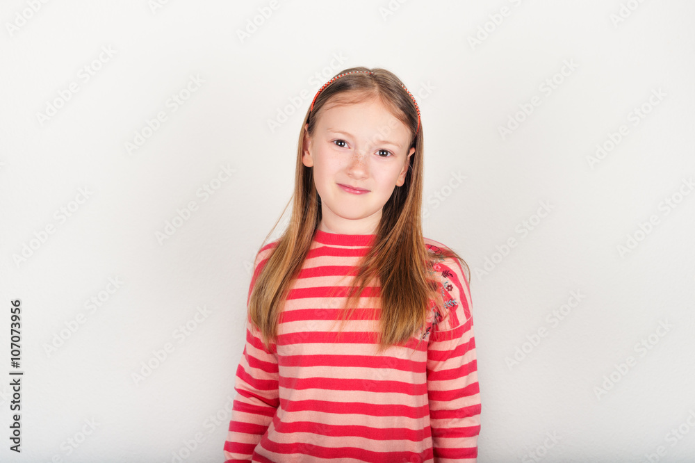 Studio portrait of adorable little girl of 8-9 years old, wearing coral color stripes pullover, standing against white background Studio portrait of adorable little girl of 8-9 years old, wearing coral color stripes pullover, standing against white background