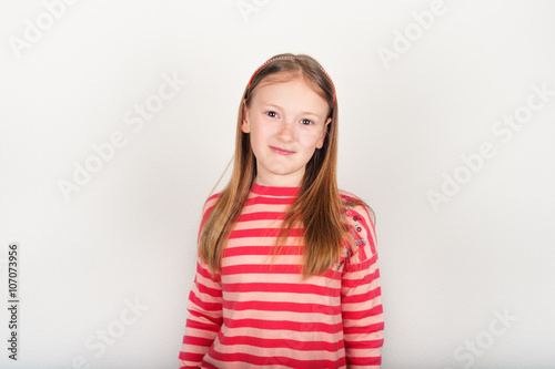 Studio portrait of adorable little girl of 8-9 years old, wearing coral color stripes pullover, standing against white background