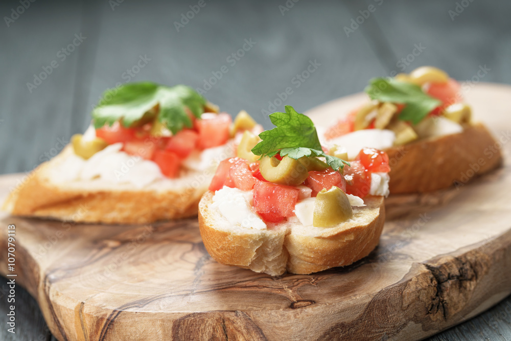 crostini with tomato, mozzarella and olives on wooden table