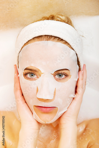 Woman sitting in bath with face mask