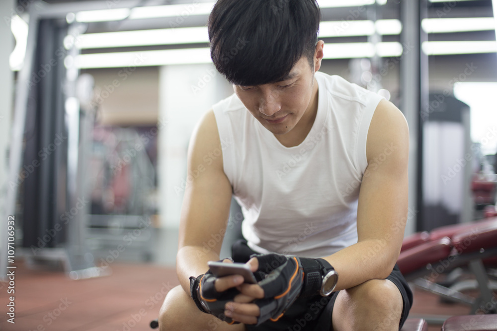 young handsome asian man using smart phone in modern gym