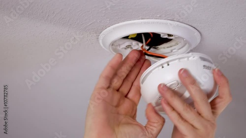 Close up of a hand installing a smoke detector and alarm in a ceiling in the USA.  Finger then presses button to test alarm.  Originally recorded in 4K