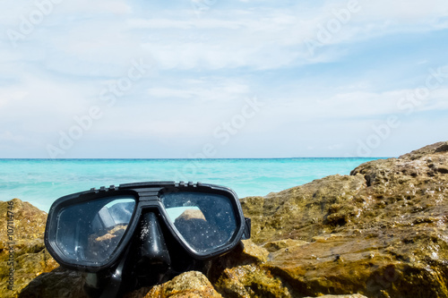 Vacation Start Here Concept, Scuba Diving Equipment On The Sea Rock of The Beach at The Corner with Crystal Clear Sea and Sky in Background as Copyspace used as Template to input Text