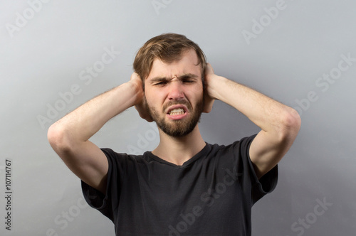 stressed young man close his ears and eyes on grey background