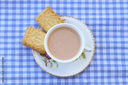 Traditional milky tea served in a bone china cup and saucer with custard cream type biscuits