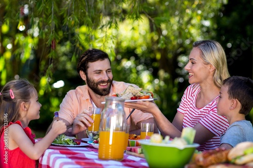 Mother offering salad while family sitting at table 