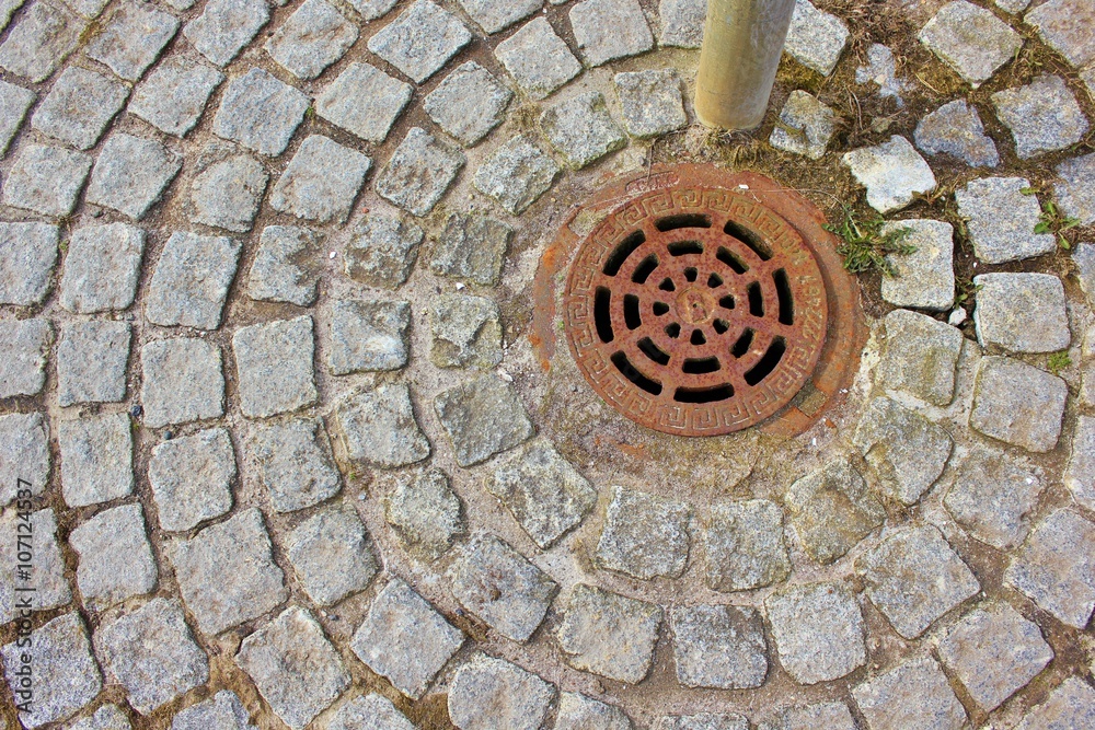 Rusty rain drainage surrounded by grey tiles in a circular pattern
