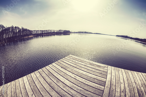 Old film stylized fisheye lens image of a wooden pier at sunset. photo