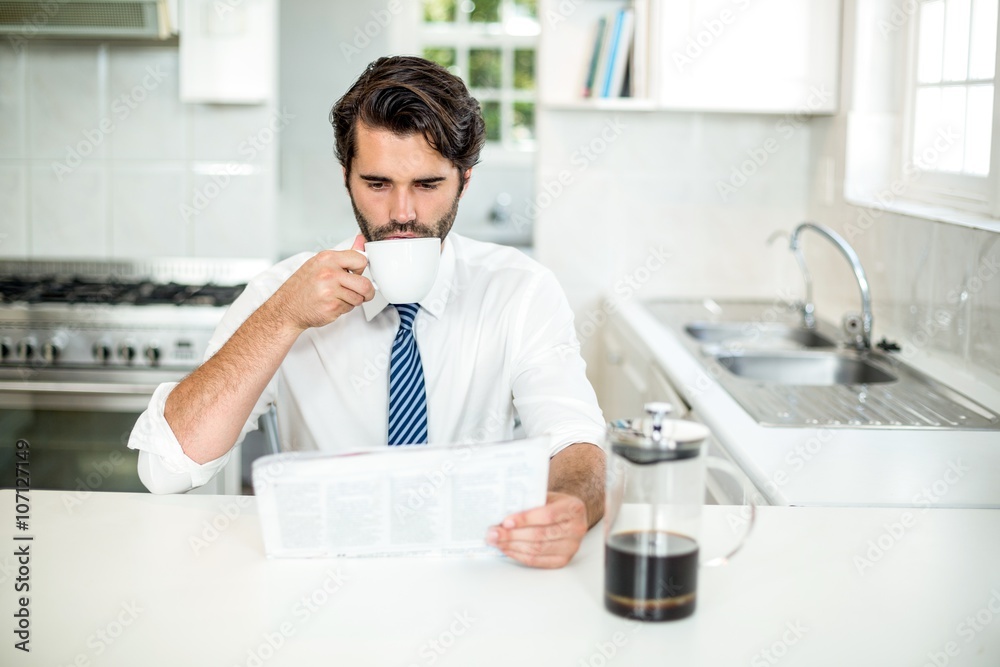 Businessman reading newspaper while drinking coffee at table