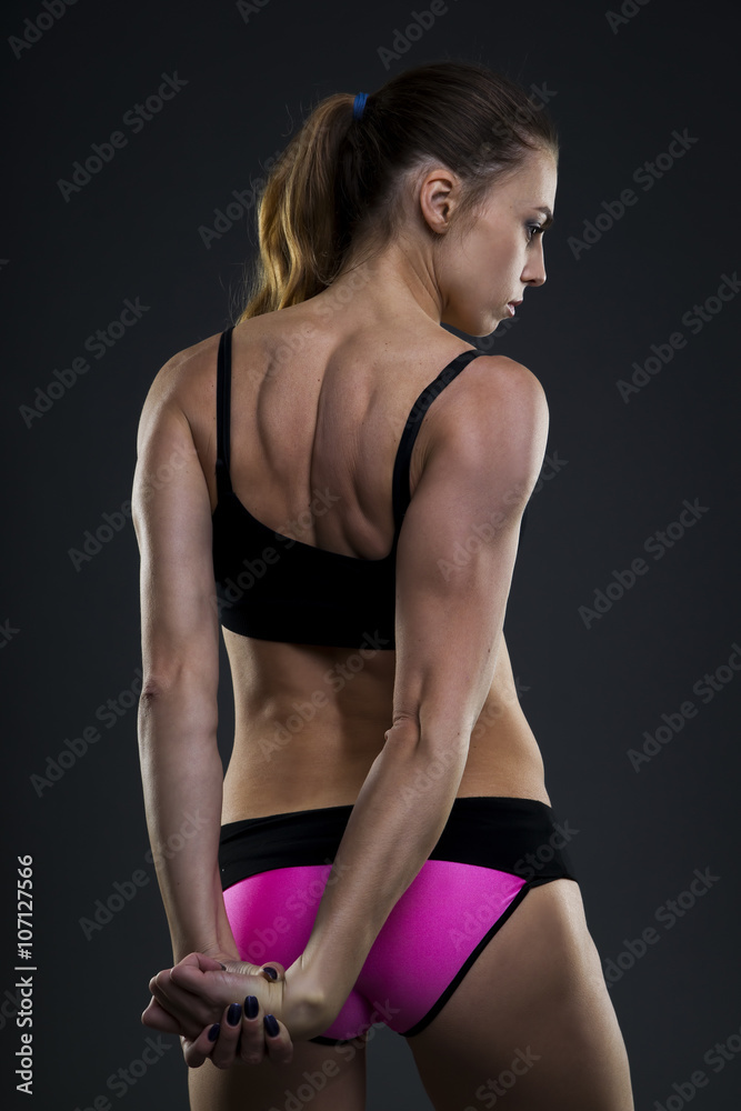 Attractive fitness woman on gray background in studio. Muscular back close-up