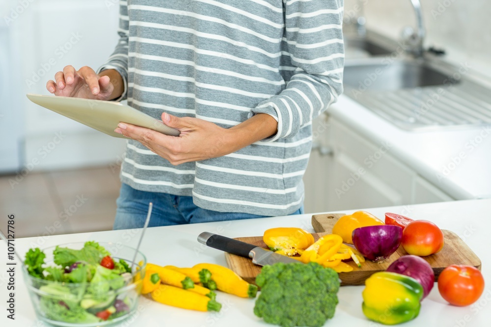 Woman using digital tablet by vegetables in kitchen Woman using digital tablet by vegetables in kitchen