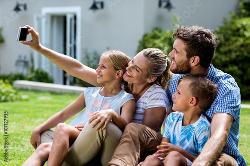 Happy mother taking selfie with family while sitting in yard 