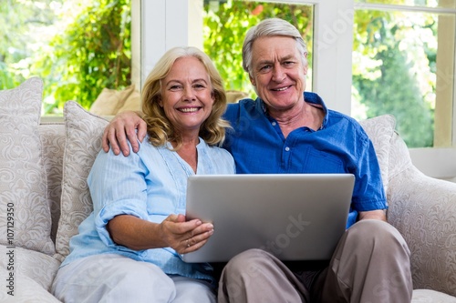 Senior couple holding laptop while sitting on sofa at home