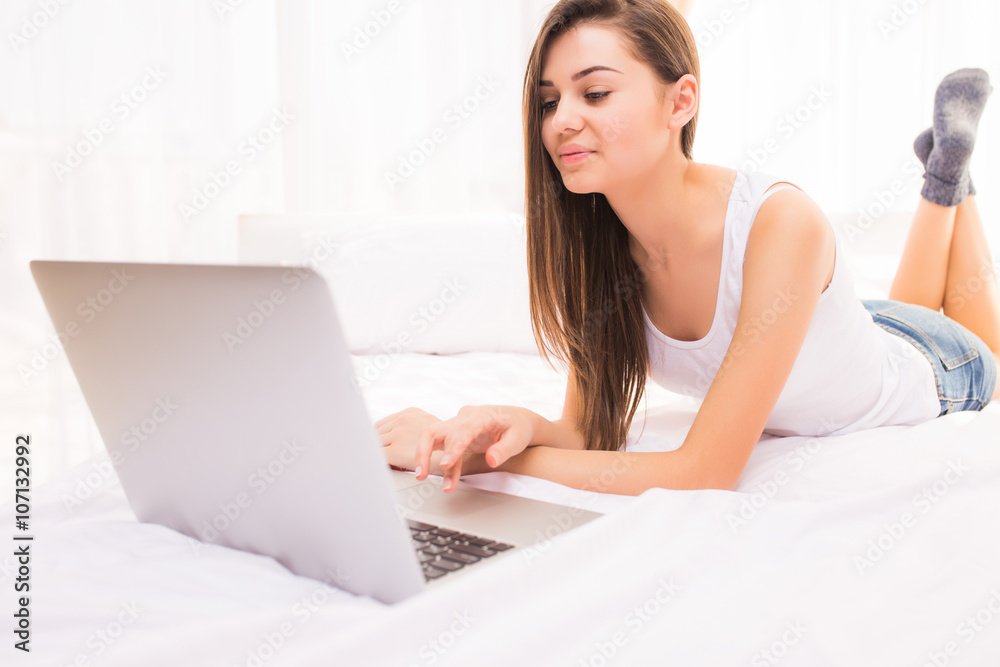 A close up shot of a smiling woman lying on her bed with her laptop in front of her. A close up shot of a smiling woman lying on her bed with her laptop in front of her.