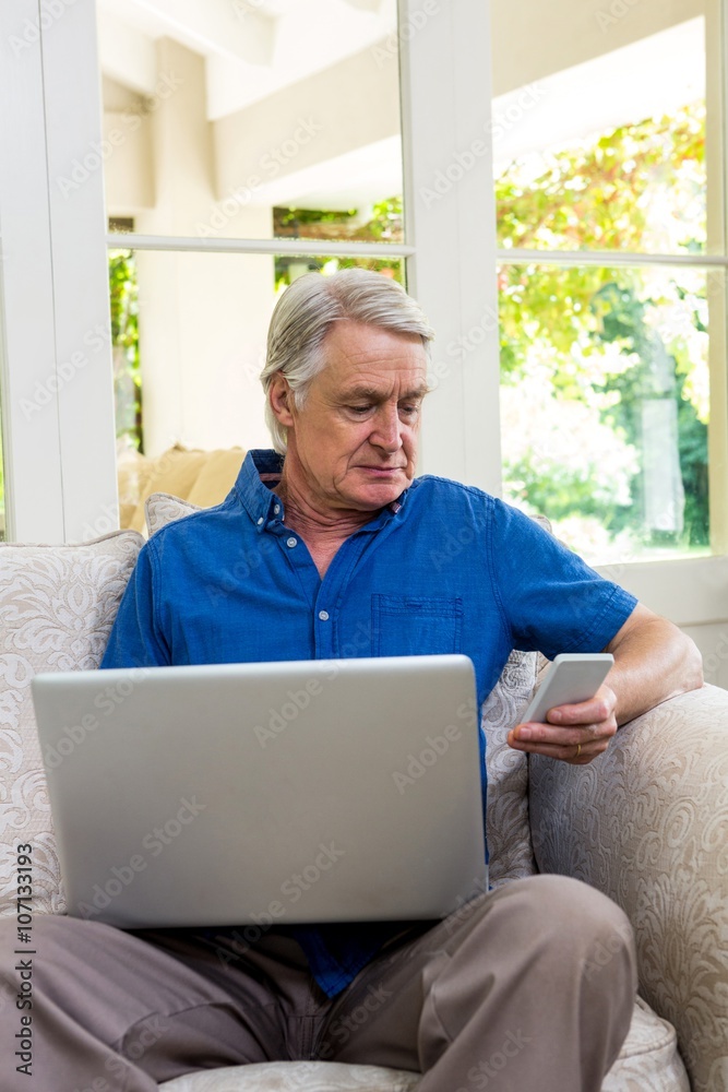 Senior man using mobile phone while working on laptop Senior man using mobile phone while working on laptop
