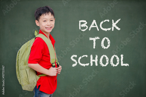 Young Asian schoolboy with backpack standing in front of chalkbo photo