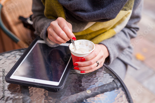 Girl stiring her coffee in the park. Tablet pc on the table. Clo photo