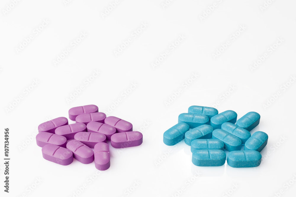 Two heaps of pink pills and blue pills side by side on white background from above high angle Two heaps of pink pills and blue pills side by side on white background from above high angle
