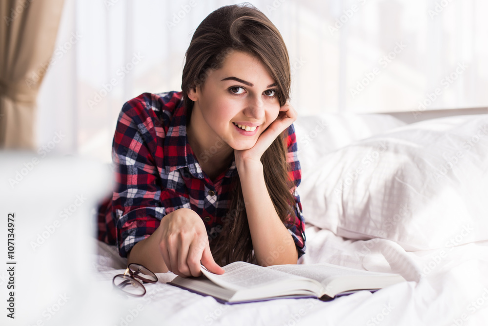 Girl reading a book in bed, lying on her stomach smiling happy and relaxed on a leisure day at home. Girl reading a book in bed, lying on her stomach smiling happy and relaxed on a leisure day at home.