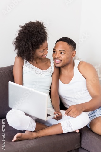 Happy couple sitting on sofa and using laptop