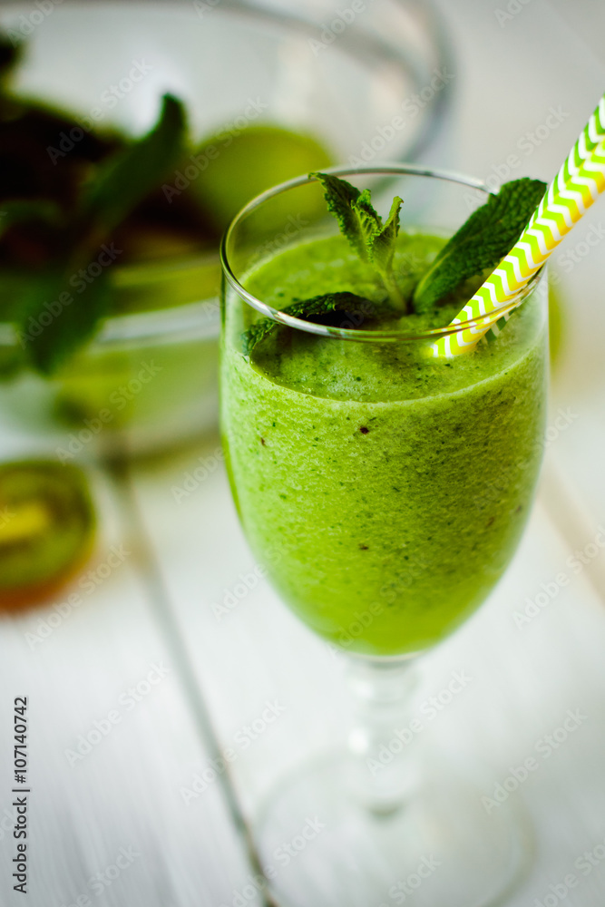 Healthy green smoothie from apples, spinach and kiwi with mint in a glass with a straw on wooden white table Healthy green smoothie from apples, spinach and kiwi with mint in a glass with a straw on wooden white table