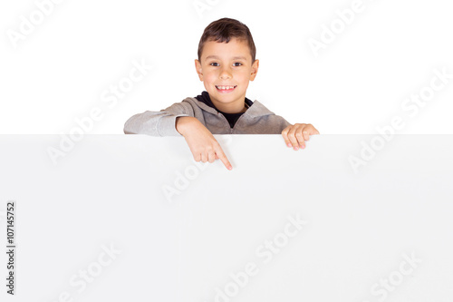 Advertising - Little kid standing behind a blank banner pointing to an advertisement isolated on white