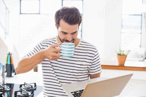 Man using laptop while having coffee in kitchen