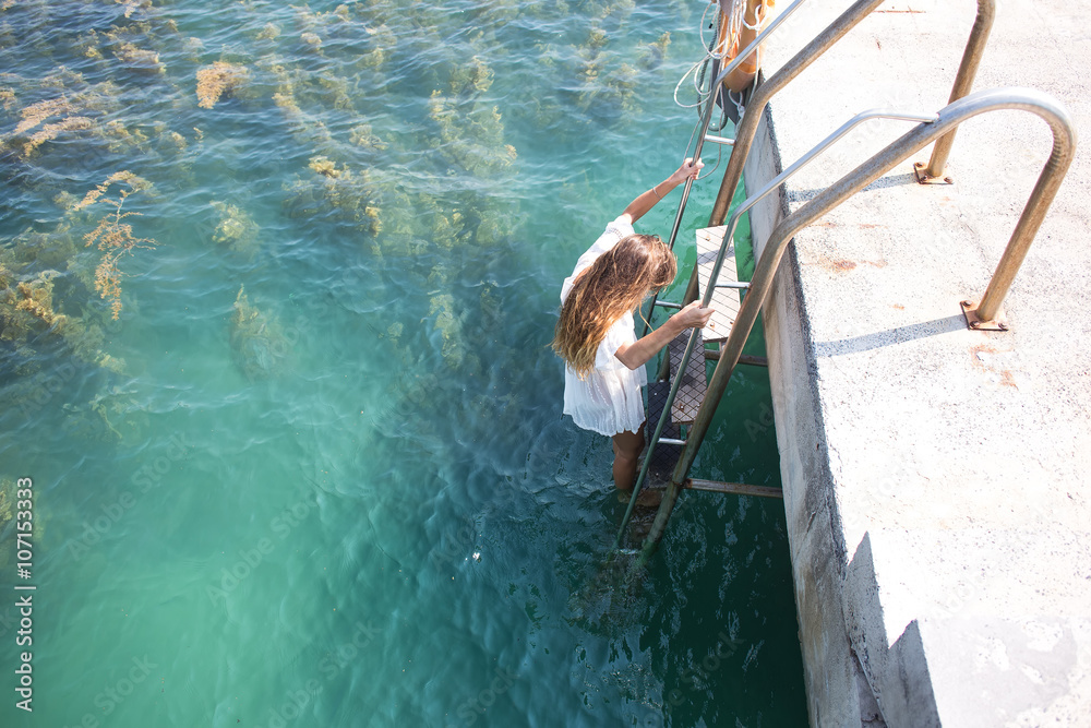 The girl jumps from a pier in water, the long-haired beautiful girl in a white dress,