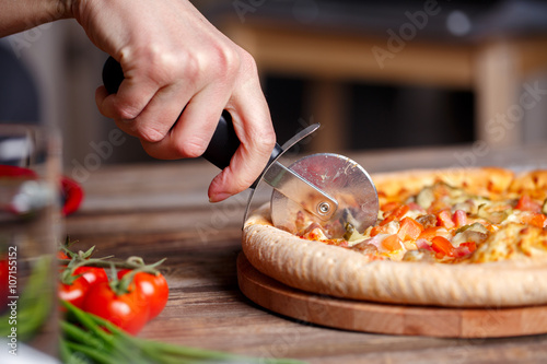 Slicing fresh pizza with roller knife. 