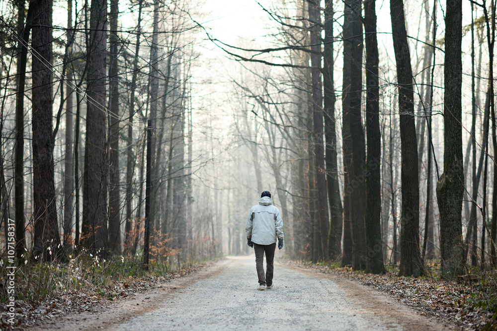 Obraz premium Man walking away down road between trees in winter forest