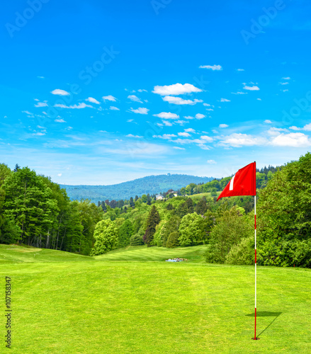 Green golf field and blue sky. Golf course red flag