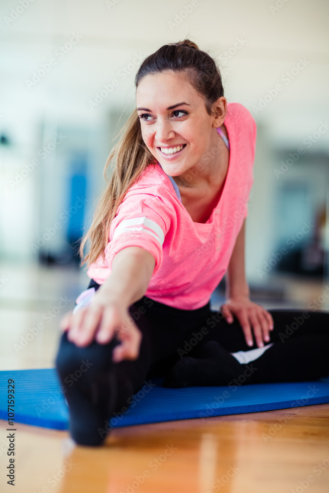 Young brunette european white caucasian girl exercising alone in gym with wooden floor doing yoga, pilates and fitness exercises
