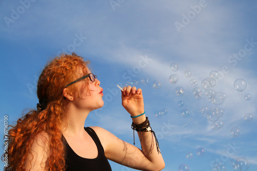 Rothaarige Jugendliche mit Brille macht Seifenblasen gegen den Himmel