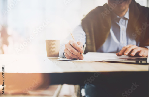 Working process. Account manager working at the wood table with new business project.Holding pencil hand, signs document and cup coffe on table. Horizontal mockup, sunny effect.Blurred, film effect