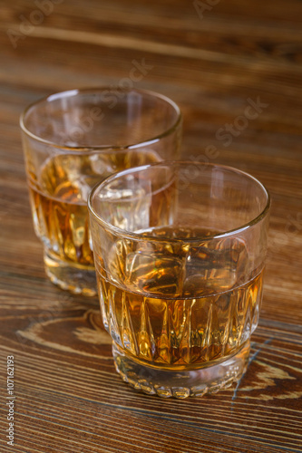 Glasses of whiskey with ice on wood.
