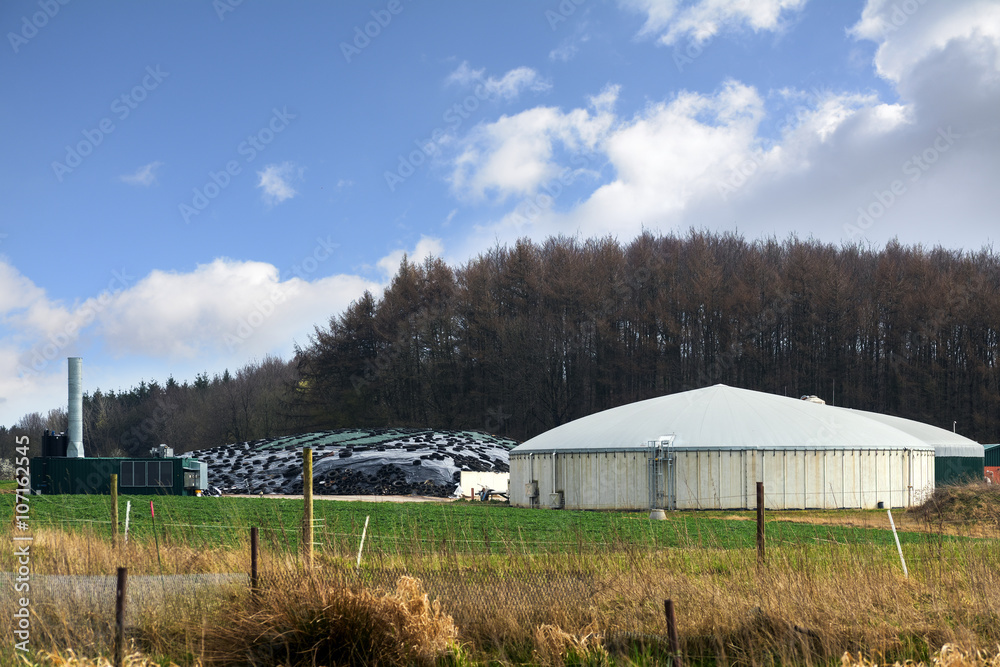 biogas plant for renewable energies between field and forest, blue sky with clouds biogas plant for renewable energies between field and forest, blue sky with clouds