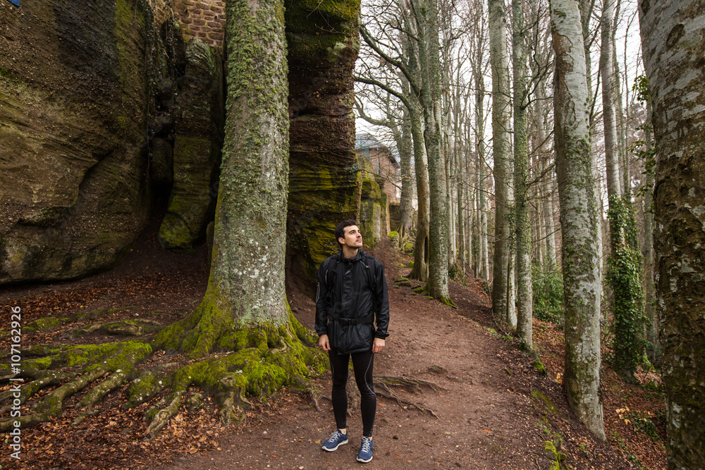 Obraz premium Young Man,Student hiking in forest.Man hiker smiling happy portrait looking up enjoying nature on foggy day during a trekking trip. Back of a young man outdoors in nature on a hiker path in forest.