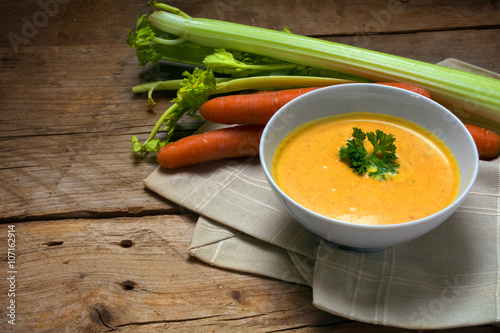 carrot soup with cream and parsley garnish in a bowl on a rustic wooden table, copy space