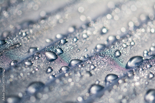 Water droplets on corrugated plastic with refracted light shinning through them at sunrise