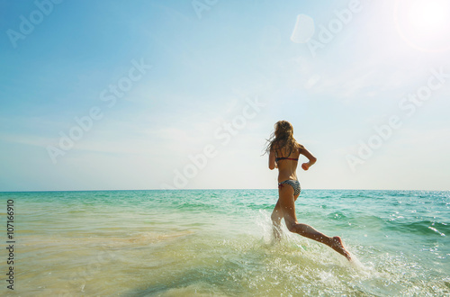 Young woman hight speed running into sea with splashes with sky  background. © upslim