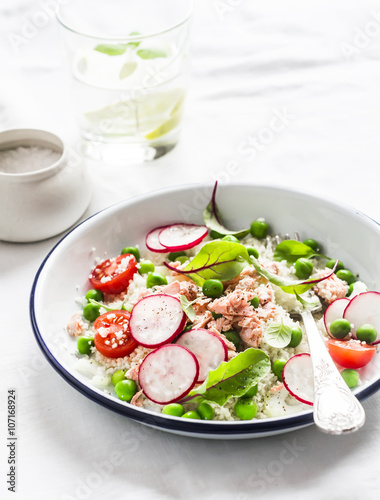 Delicious healthy food - salad with cous cous, fresh vegetables and baked salmon. On a light background