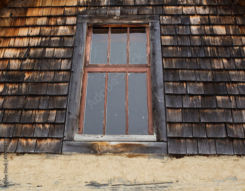 Fotografia Old wood framed window in exterior top floor of decaying wood slat wall