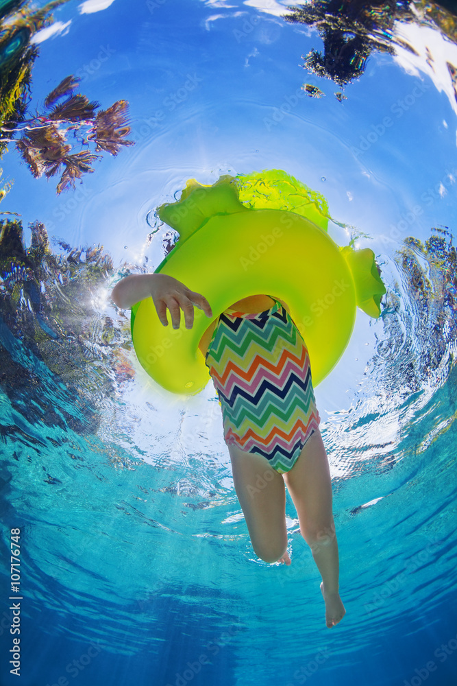 Funny underwater photo of baby girl swimming with fun on inflatable frog  tube in clear aqua park pool. Healthy family lifestyle, children outdoor  water sports activity with parents on summer holidays. Stock