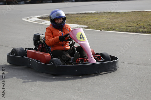  girl is driving Go-kart car with speed in a playground racing track.