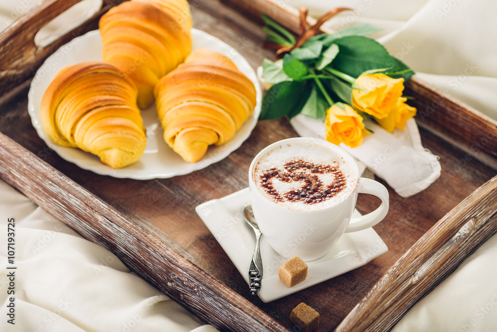 Coffee, croissant and flowers on tray on a wooden table Coffee, croissant and flowers on tray on a wooden table
