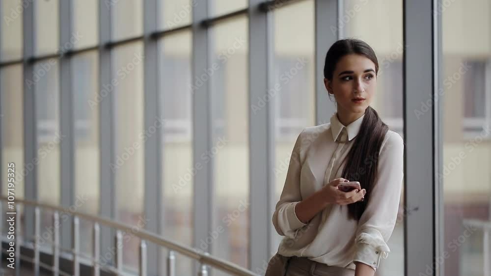 Elegant woman using mobile phone standing in office interior Elegant woman using mobile phone standing in office interior