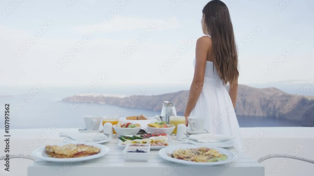 Breakfast table and luxury travel woman on santorini. Well balanced perfect breakfast table served at resort. Female tourist is looking at beautiful view of sea and caldera enjoying her vacation.